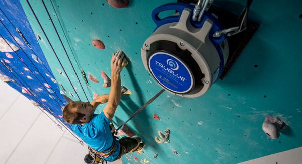 Man climbing on a blue indoor climbing wall with a TRUBLUE Auto Belay