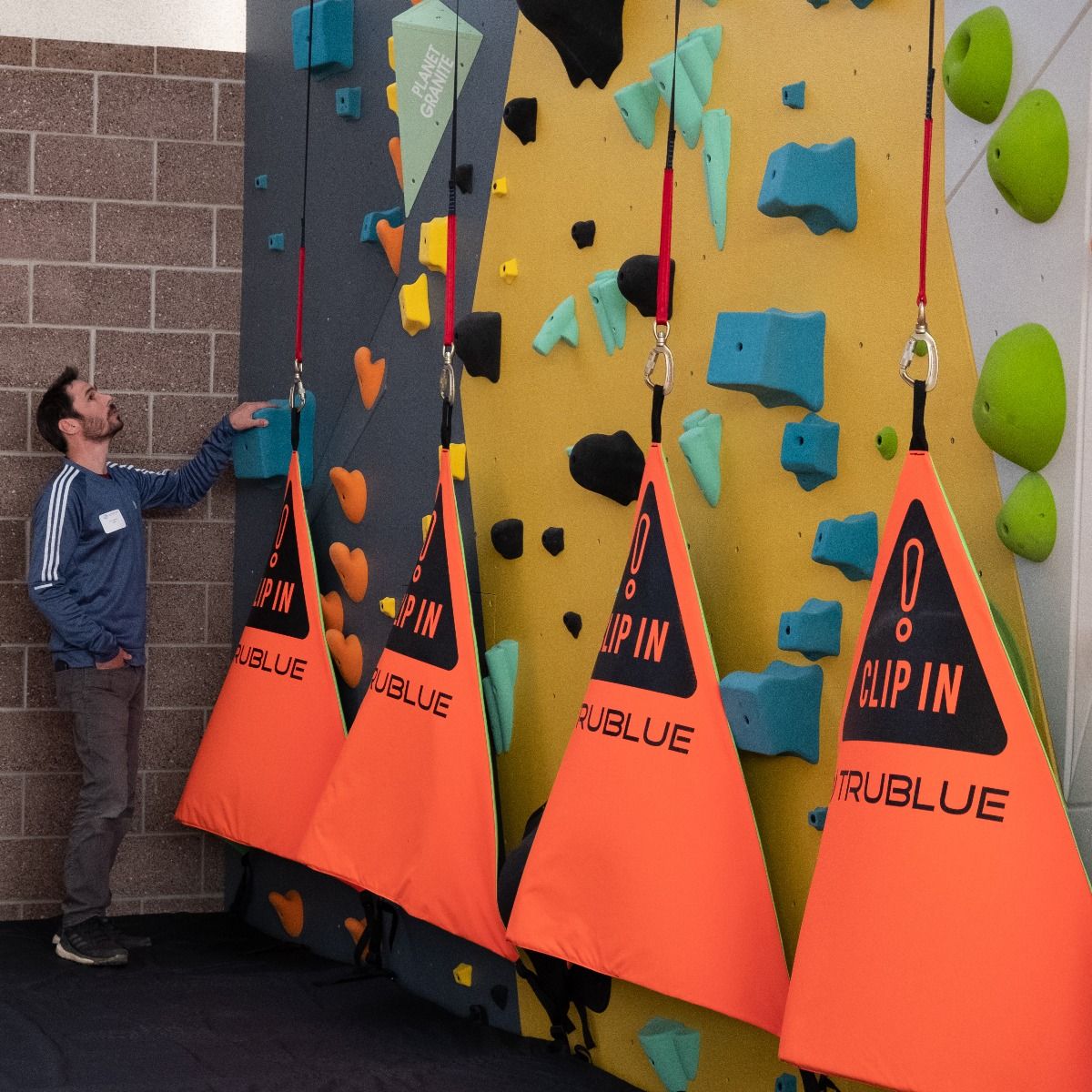 Kevin Jorgeson standing in front of a indoor rock climbing wall with auto belays and belay gates.
