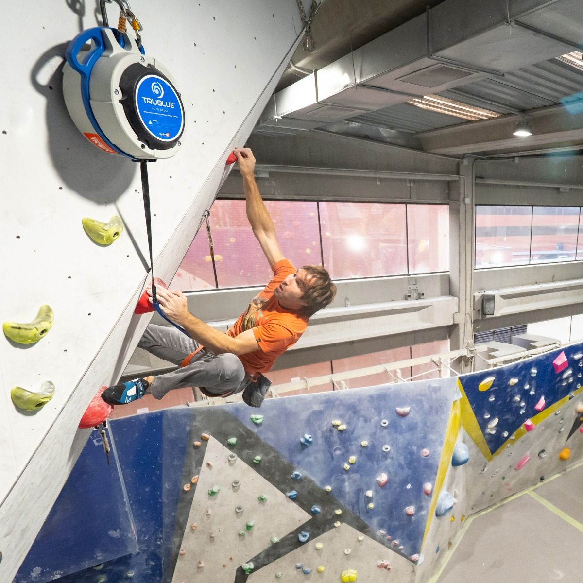 Chris Sharma climbing on a TRUBLUE Auto Belay in an indoor rock climbing gym.
